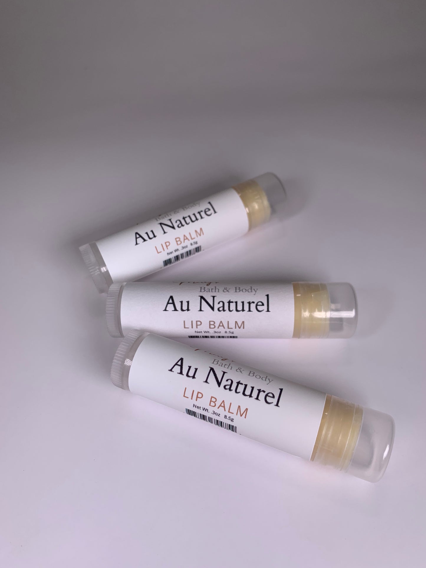 Three lip balms laying down so the name is clearly displayed.  Au Naturel flavor. 