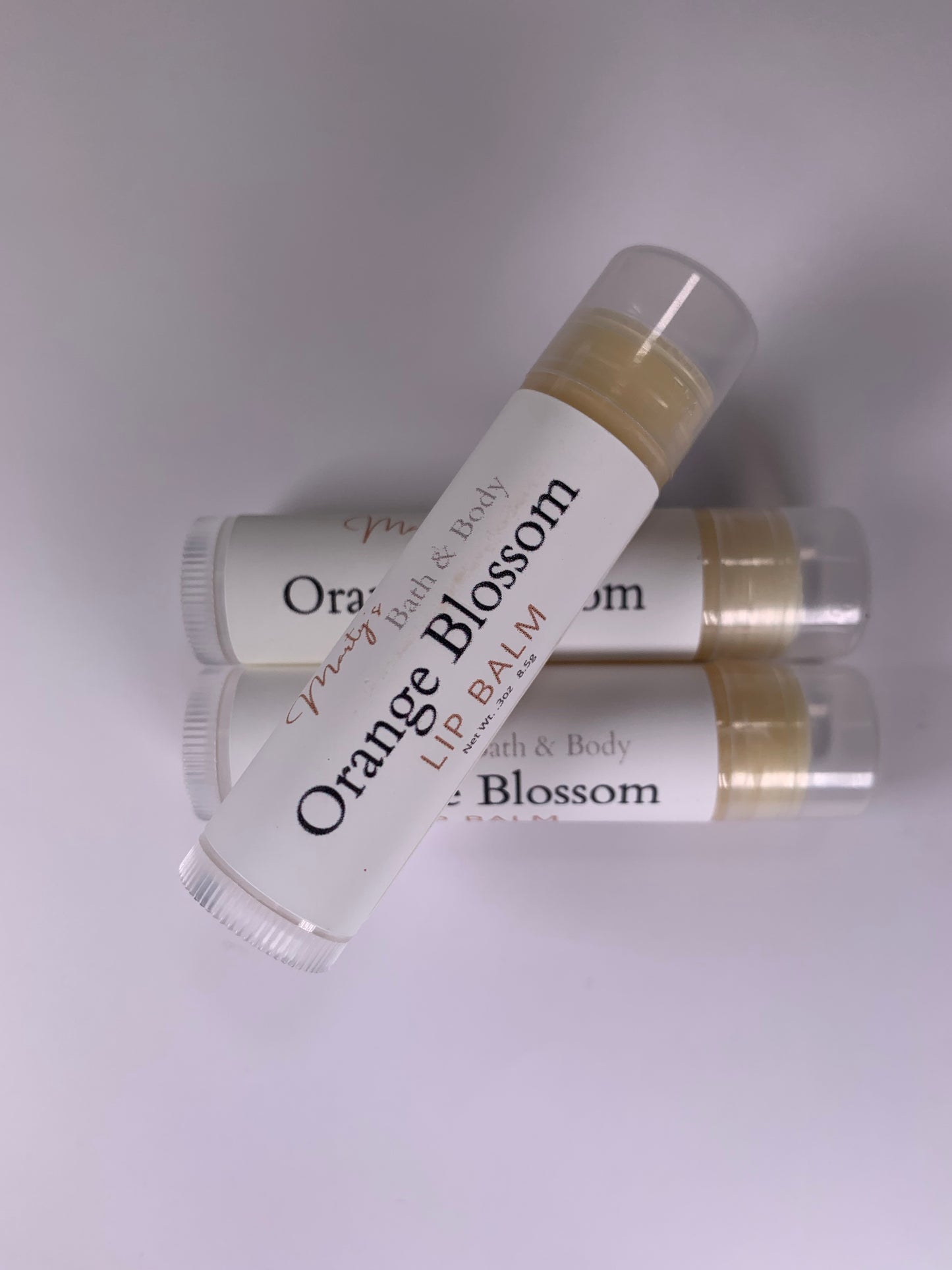 Three tubes of Orange Blossom handmade lip balm with one shown up close.