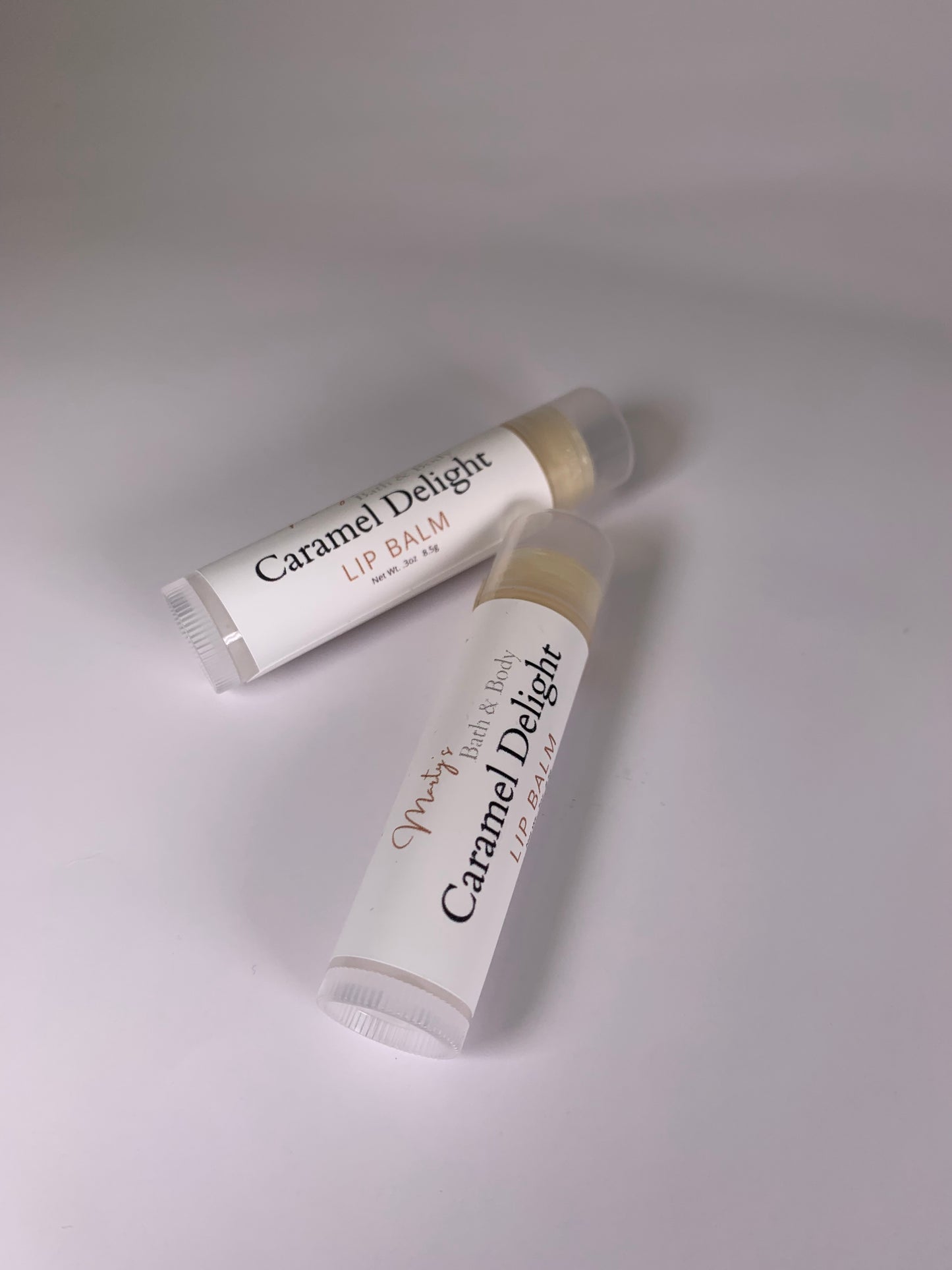 Caramel Delight Lip Balm. Two caramel flavored lip balms laying down to display the labels. All vegan ingredients.