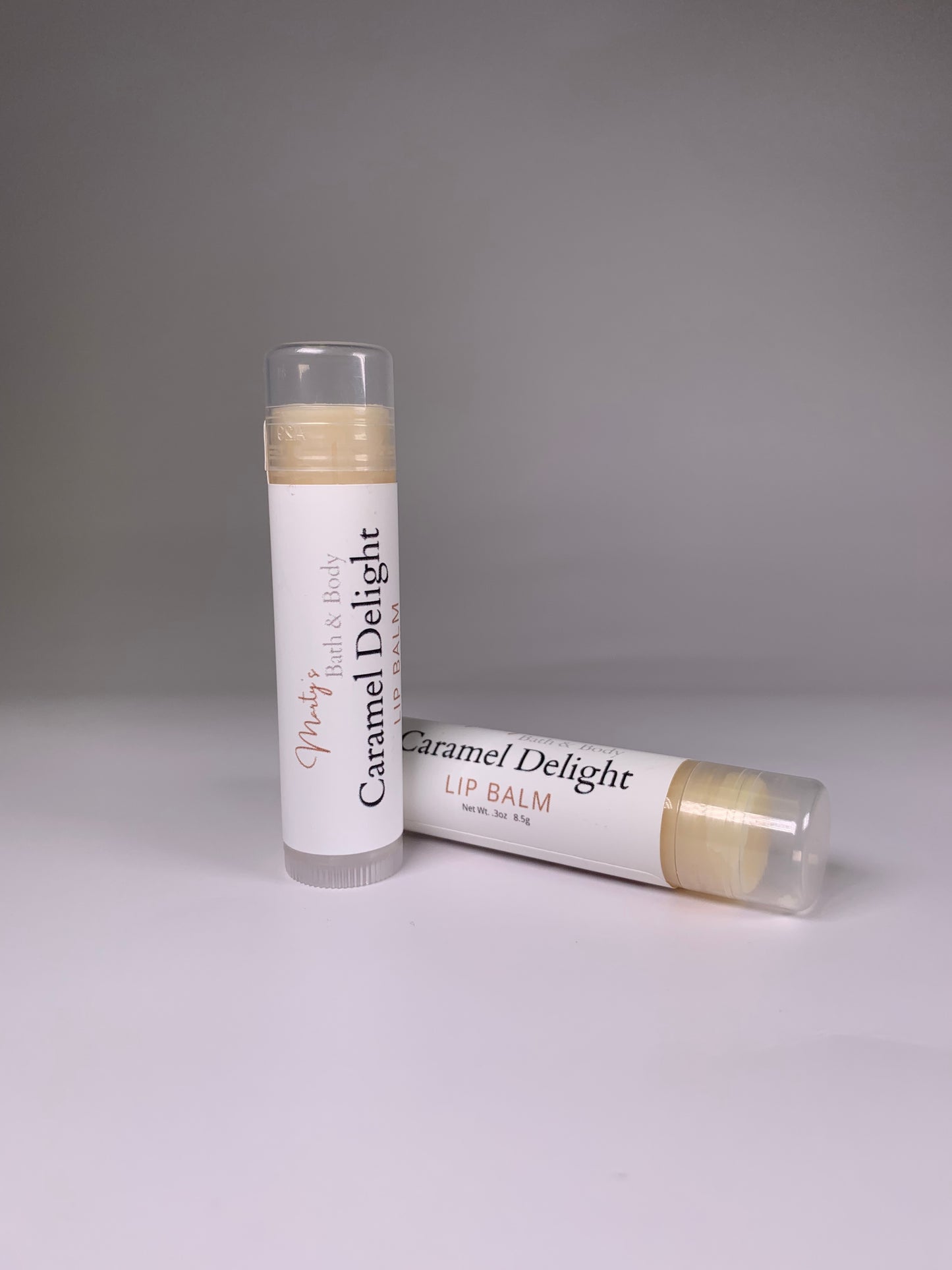 Caramel Delight Lip Balm. Two caramel flavored lip balms with one laying down while the other is standing slightly in front of the other. Handmade and all natural.